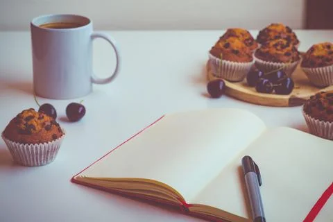 An empty notebook with a red cover lying on a table next to a pen, a cup of c Stock Photos