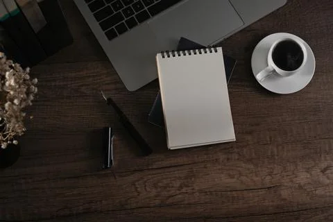 Empty notepad, laptop computer, coffee cup and flower pot on wooden desk. Flat Stock Photos