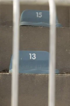 Empty numbered blue stadium seats seen through metal railings Stock Photos