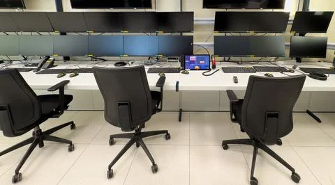 Empty office chairs face a wall of computer monitors Stock Photos