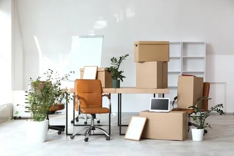 Empty office space with moving boxes, desk, chairs, and plants for relocation Stock Photos