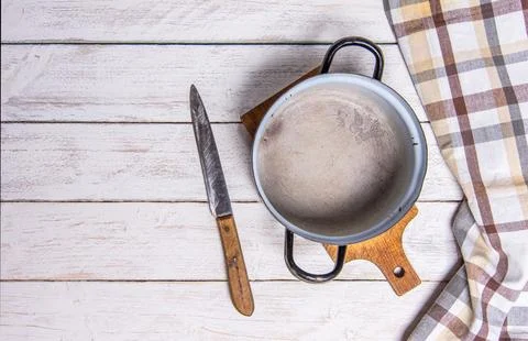 Empty old enamel pot and rustic knife on white boards. Checkered table cloth on Stock Photos