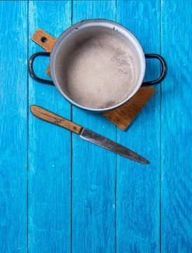 Empty old enamel pot and rustic knife on navy blue boards. Copyspace. Vertical Stock Photos
