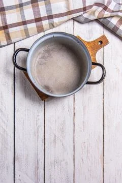 Empty old enamel pot on white boards. Checkered table cloth on top side Foto stock