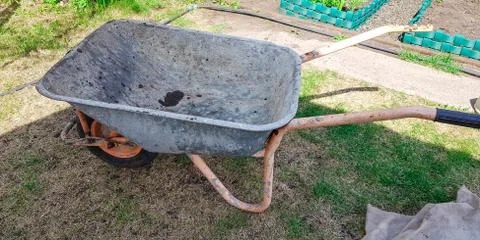 An empty old wheelbarrow on the garden plot stands on the grass. Transportati Stock Photos