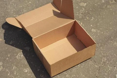 An empty open brown cardboard box sitting on a textured asphalt surface Stock Photos