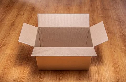 An empty open cardboard box sits on a polished wooden laminate floor Stock Photos