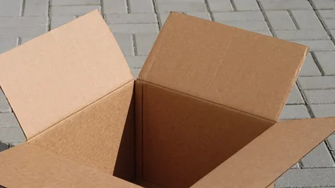 An empty open cardboard box sitting on a grey paved outdoor surface. Stock Footage 331885299