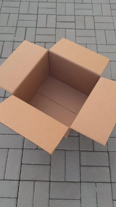 An empty open cardboard box sitting on a grey paved outdoor surface. Stock Footage 331938757
