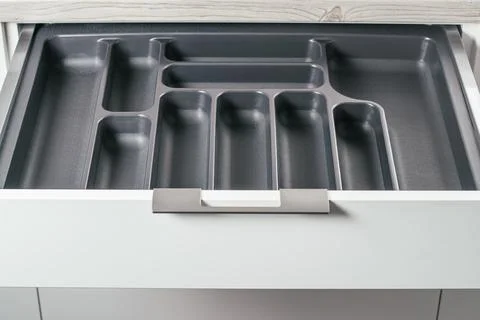 Empty open drawer of white kitchen set with black cutlery organizer tray. Sto Stock Photos