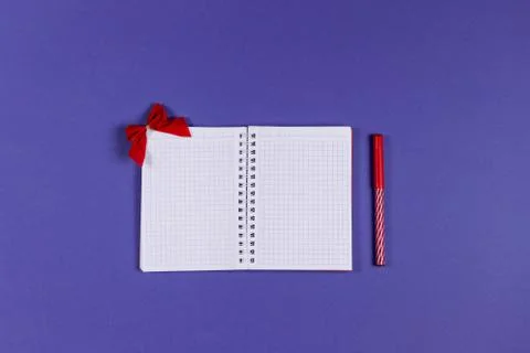 Empty open notepad with red marker and bow on the violet background. Fotos de archivo