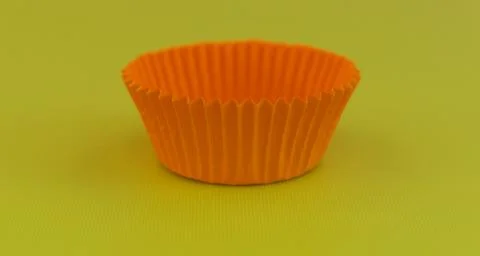Empty orange cup cake case against plain green yellow background with copy sp Stock Photos