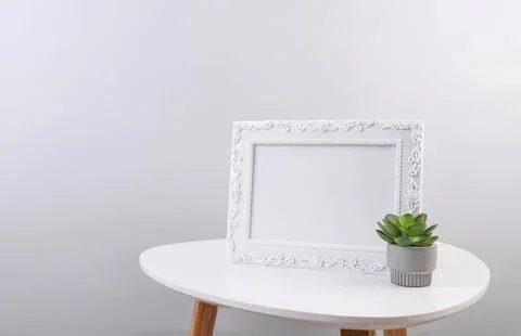 Empty ornate frame on white table with green plant Stock Photos