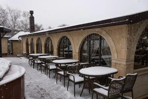 Empty outdoor cafe with large windows, with snow-covered tables and chairs Stock Photos