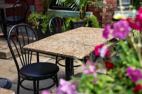 Empty outdoor cafe patio table beside pink flowers Stock Photos
