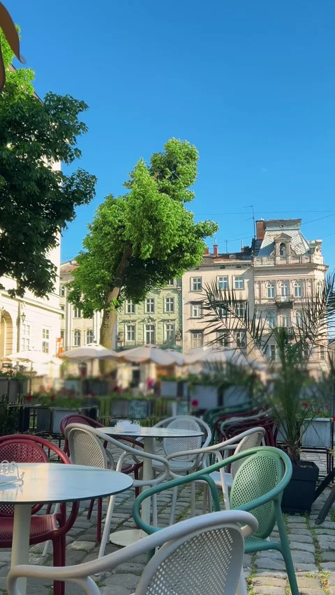 Empty outdoor cafe tables and chairs sit on a sunlit city street. Stock Footage 339085377