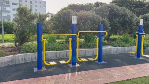 Empty Outdoor Exercise Equipment Surrounded by Greenery and High-Rises Stock Footage 340153388