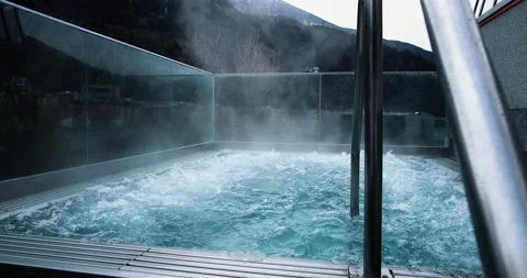 An empty outdoor jacuzzi with steam. We can see mountains in the background, per Vídeos de archivo 143631320