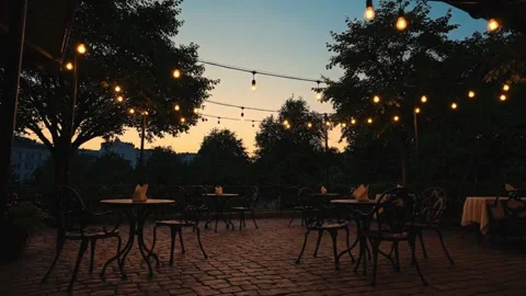 Empty outdoor terrace cafe tables illuminated by warm hanging string lights at 動画素材 344646963