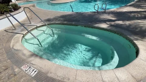 Empty Oval Hot Tub with Bubbling Turquoise Water Beside Resort Pool Stock Footage 345369807
