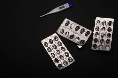 Empty packages of tablets and a thermometer on a black background Stock Photos