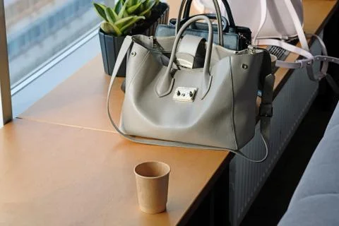 An empty paper cup on the table and a gray women bag nearby. Stock Photos