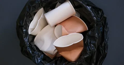 Empty paper cups fall into the trash can with a black plastic bag Stock Footage 235585388