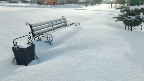Empty park bench and trash bin covered in deep pristine white snow on a clear Stock Footage 341657456