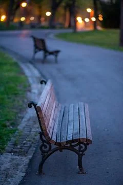 Empty park bench on curved path at dusk with bokeh lights Stock Photos