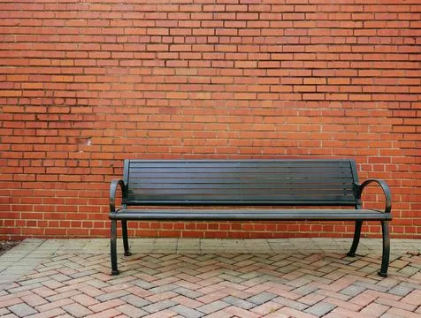 An empty park bench in front of a blank brick wall Stock Photos