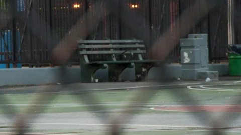 Empty park bench on side of basketball court with fence in foreground, day. Video stock 108399922