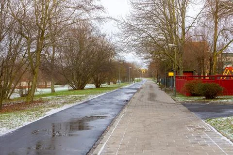 Empty park pathway with bare trees and patches of snow in late autumn Stock Photos