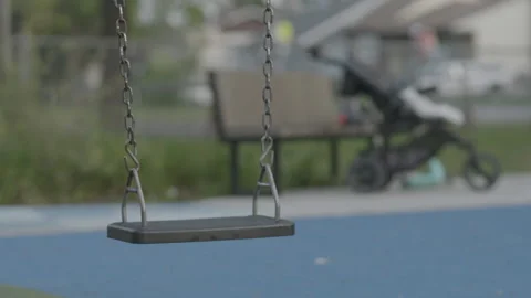 Empty park swing swaying slowly with off focus stroller in background Vídeos de archivo 231356235