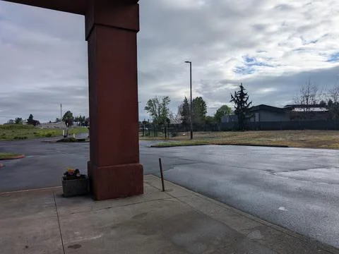 Empty parking lot beside an open field under layered clouds and patches Stock Photos