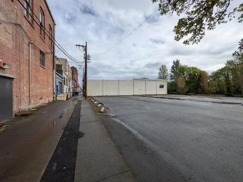 Empty parking lot beside a plain white industrial building, green trees Stock Photos