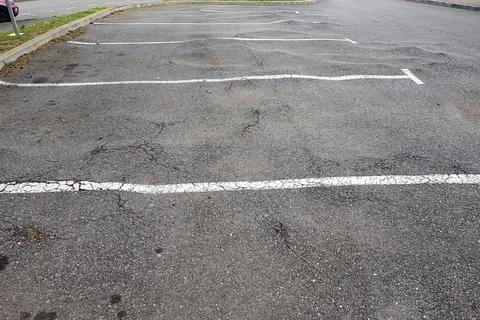 An empty parking lot features multiple cracked asphalt surfaces by trees root Stock Photos