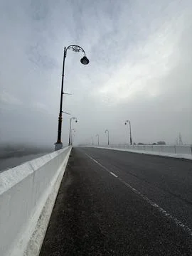 Empty paved bridge disappearing into dense morning mist with vintage lamp pos Stock Photos