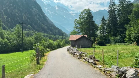 Empty paved path curves through green farmland in Lauterbrunnen outdoors, Swiss Vídeos de archivo 345035328