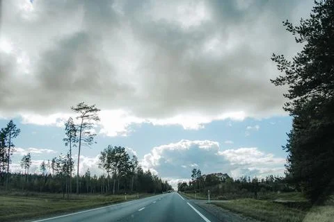 Empty paved road leading through a forested landscape beneath dramatic stor.. Stock Photos