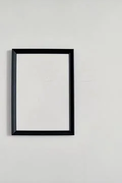 An empty photo frame with a black border hanging on a white wall Stock Photos