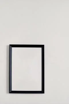 An empty photo frame with a black border hanging on a white wall Stock Photos