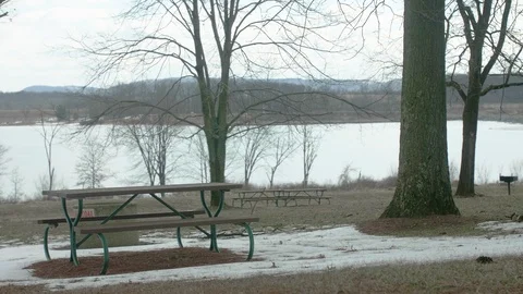 Empty Picnic Tables at Park in Winter with Lake in Background PAN LEFT Video stock 104725417