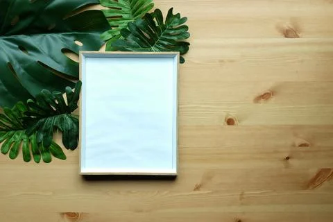 Empty picture frame and green leafs on wooden background. Stock Photos