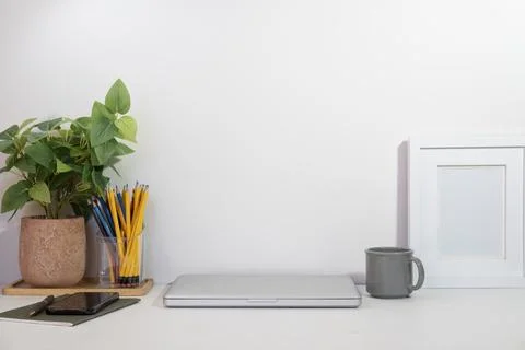 Empty picture frame, laptop, coffee cup and houseplant on white office desk. Stock Photos