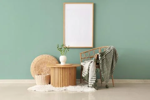 Empty picture frame on a mint green wall with a rattan chair, wooden table, a Stock Photos