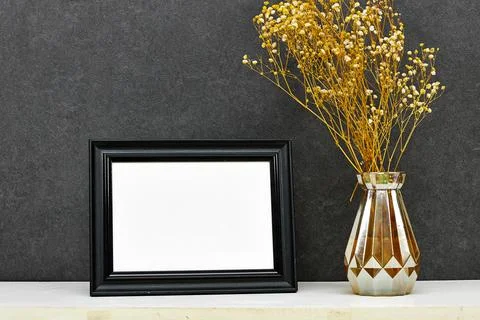 Empty picture frame mockup and gypsophilavase on wooden table near grunge wall,  Stock Photos