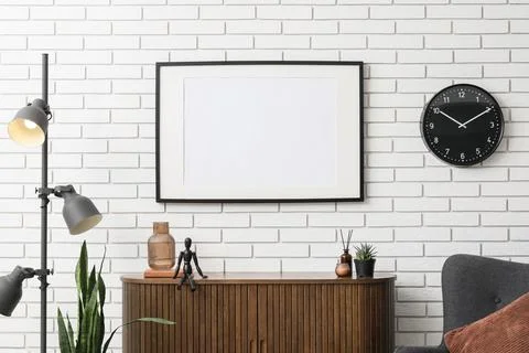 Empty picture frame on a white brick wall with a modern wooden cabinet and fl Stock Photos