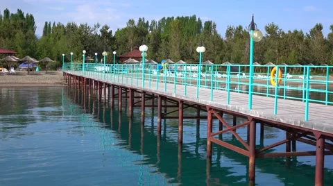 Empty pier, cane sun umbrellas and sunbeds against trees. 4K low season video Stock Footage 64026886