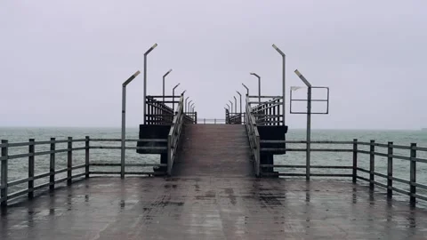 Empty pier extends into sea under grey sky, reflecting serene and moody Stock Footage 274703509