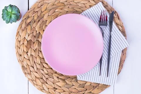 Empty pink plates, a knife and a fork on a straw eco-friendly napkin. Stock Photos